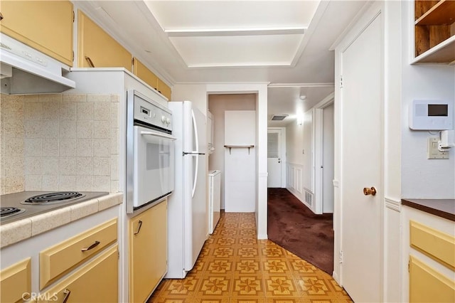 kitchen with white appliances, visible vents, under cabinet range hood, tile counters, and backsplash