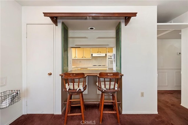 interior space featuring a breakfast bar, cream cabinets, backsplash, carpet floors, and under cabinet range hood