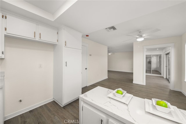 kitchen featuring dark wood-type flooring, light stone counters, white cabinets, and ceiling fan