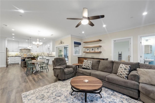 living room with ceiling fan with notable chandelier, ornamental molding, and light hardwood / wood-style floors