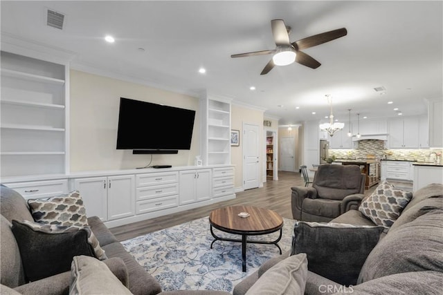 living room with hardwood / wood-style floors, crown molding, ceiling fan with notable chandelier, and built in features