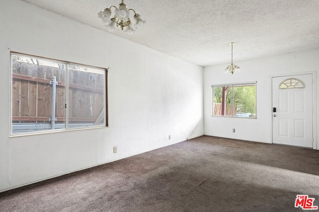 spare room with a notable chandelier, a textured ceiling, and carpet