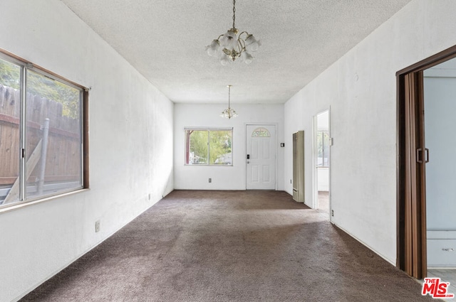 carpeted spare room with an inviting chandelier and a textured ceiling