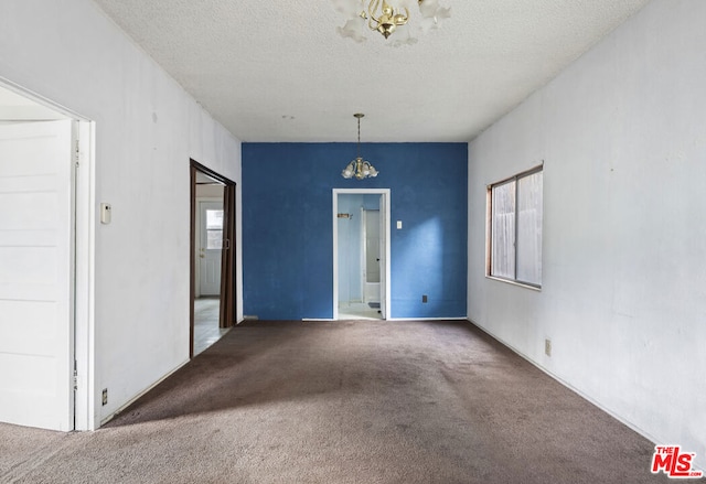 carpeted spare room featuring a textured ceiling and an inviting chandelier