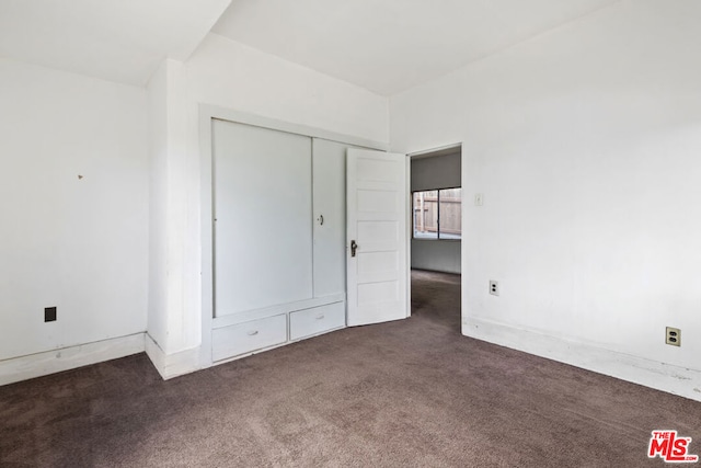 unfurnished bedroom with dark colored carpet and a closet