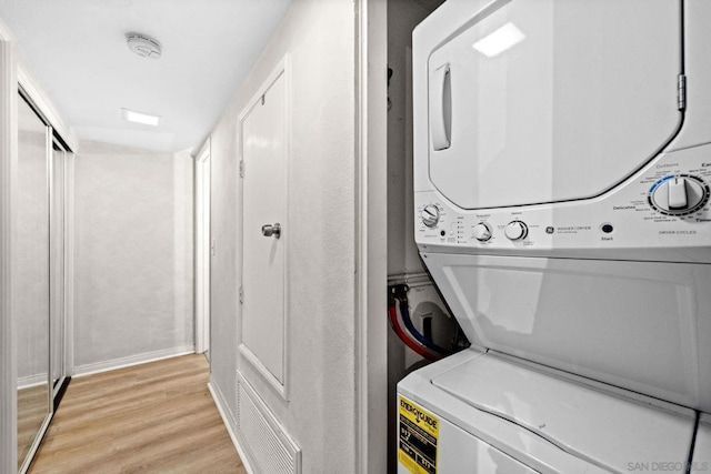 laundry area featuring stacked washer and clothes dryer and light wood-type flooring