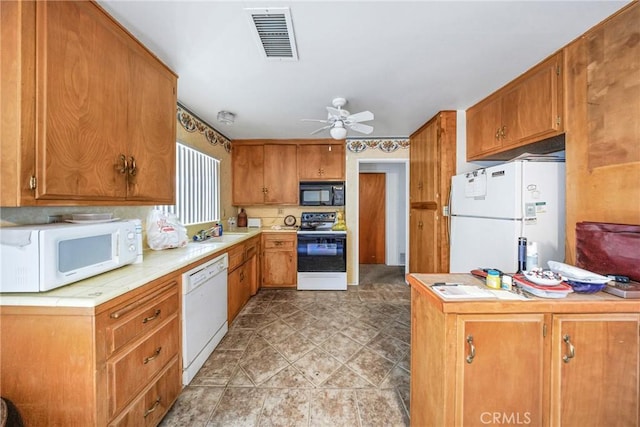 kitchen featuring brown cabinetry, visible vents, white appliances, and tile countertops