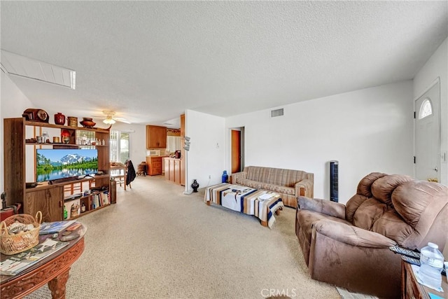 living area with a textured ceiling, visible vents, a ceiling fan, and light colored carpet