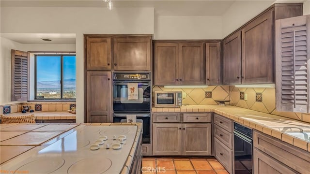 kitchen featuring white electric stovetop, tile countertops, tasteful backsplash, dobule oven black, and stainless steel microwave