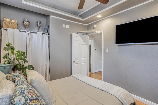 bedroom featuring crown molding, a tray ceiling, light hardwood / wood-style flooring, and ceiling fan