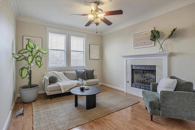 living room featuring ceiling fan, ornamental molding, hardwood / wood-style floors, and a tile fireplace