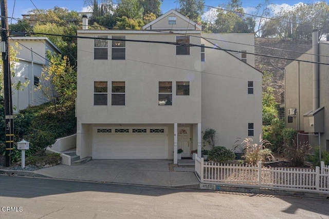 view of front facade with a garage, concrete driveway, fence, and stucco siding