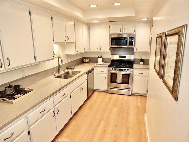 kitchen with sink, appliances with stainless steel finishes, white cabinetry, a raised ceiling, and light wood-type flooring