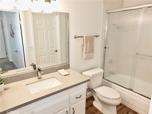 full bathroom with hardwood / wood-style flooring, vanity, bath / shower combo with glass door, and toilet