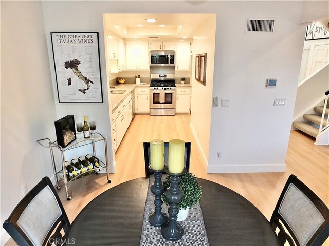 kitchen with white cabinetry, sink, light hardwood / wood-style floors, a tray ceiling, and stainless steel appliances