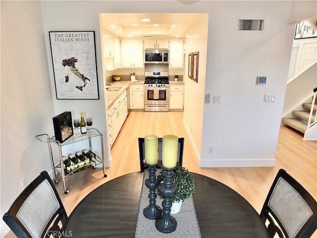 kitchen featuring sink, appliances with stainless steel finishes, a tray ceiling, light hardwood / wood-style floors, and white cabinets