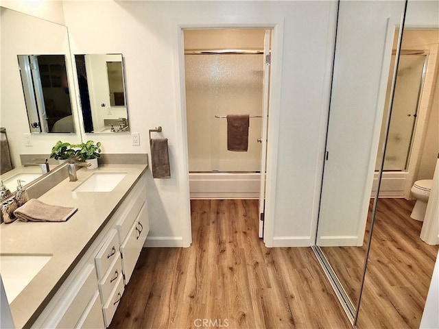 full bathroom with hardwood / wood-style flooring, vanity, combined bath / shower with glass door, and toilet