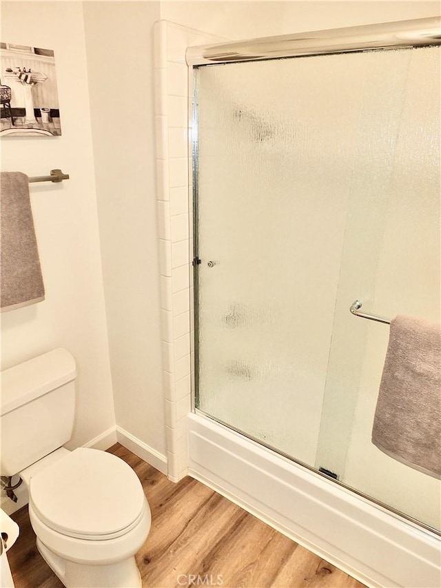 bathroom with hardwood / wood-style flooring, shower / bath combination with glass door, and toilet