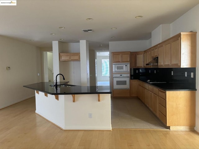 kitchen featuring sink, light wood-type flooring, a kitchen bar, a center island with sink, and white appliances