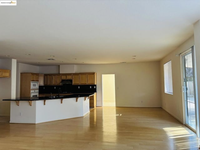 kitchen featuring white appliances, sink, a breakfast bar, and light hardwood / wood-style floors