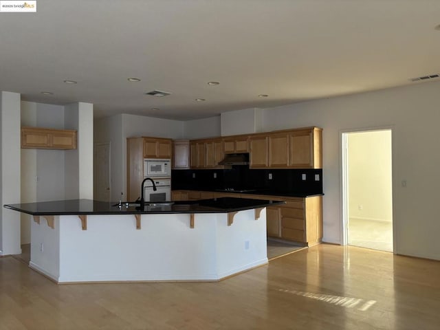 kitchen featuring light wood-type flooring, a kitchen bar, white appliances, and a spacious island