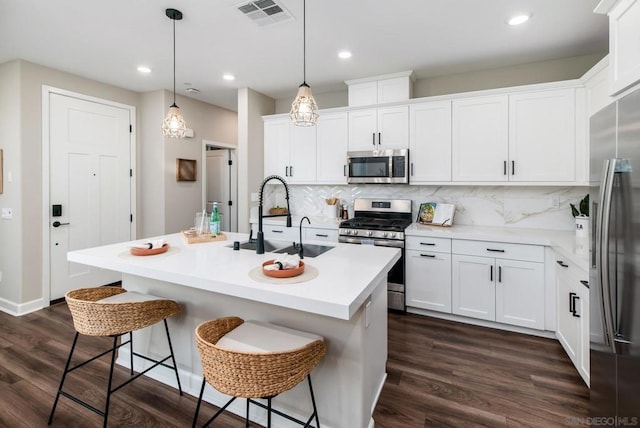 kitchen featuring a kitchen bar, a center island with sink, hanging light fixtures, appliances with stainless steel finishes, and white cabinets