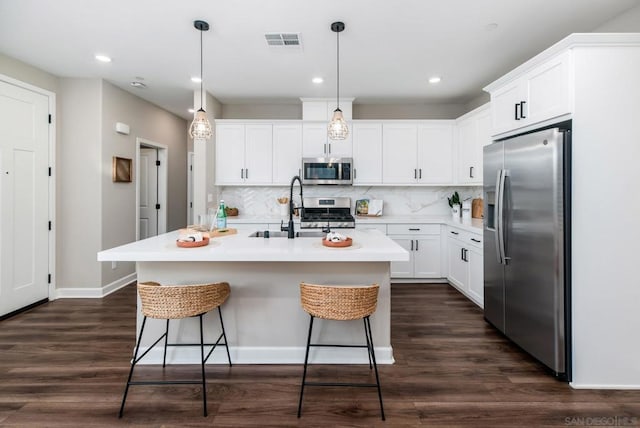 kitchen with sink, appliances with stainless steel finishes, a kitchen island with sink, hanging light fixtures, and white cabinets