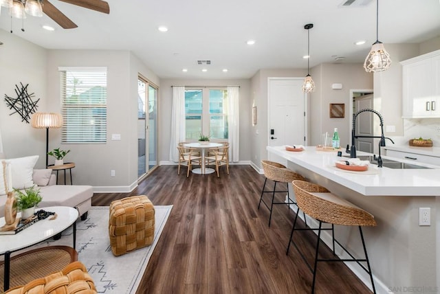 kitchen featuring sink, hanging light fixtures, a kitchen breakfast bar, dark hardwood / wood-style floors, and white cabinets