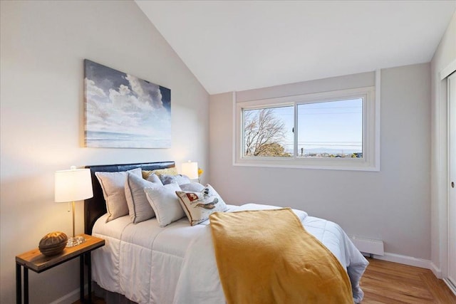 bedroom with hardwood / wood-style flooring, vaulted ceiling, and a baseboard heating unit