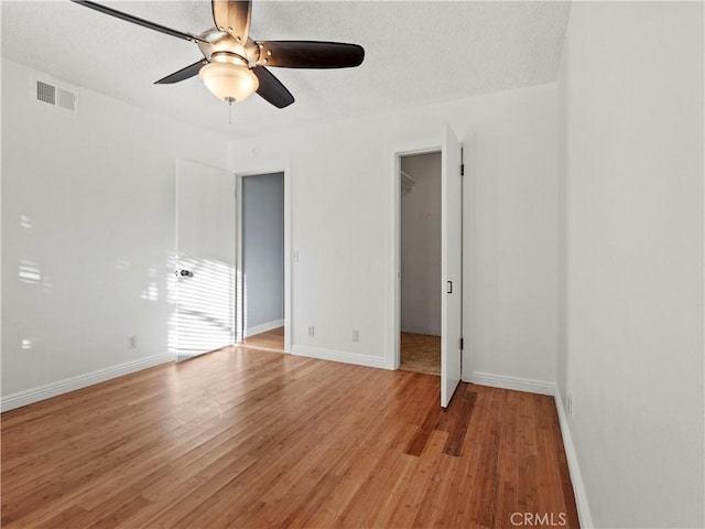 unfurnished bedroom with ceiling fan, a spacious closet, a textured ceiling, and light wood-type flooring