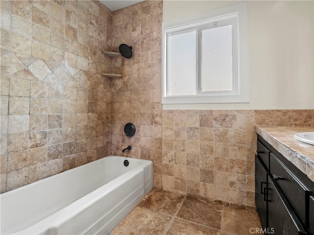 bathroom featuring tiled shower / bath combo, vanity, and tile walls