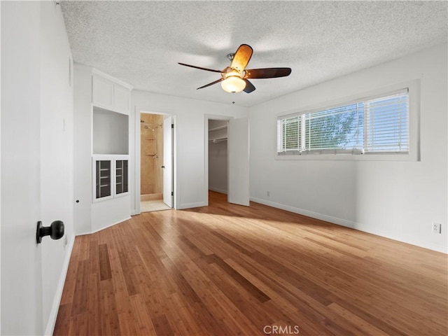 unfurnished bedroom featuring light hardwood / wood-style flooring, ceiling fan, a textured ceiling, a walk in closet, and a closet