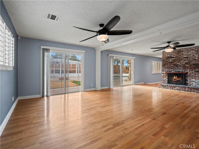 unfurnished living room featuring ceiling fan, a healthy amount of sunlight, a fireplace, and light hardwood / wood-style flooring