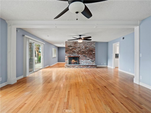 unfurnished living room with ceiling fan, a textured ceiling, a brick fireplace, and light wood-type flooring