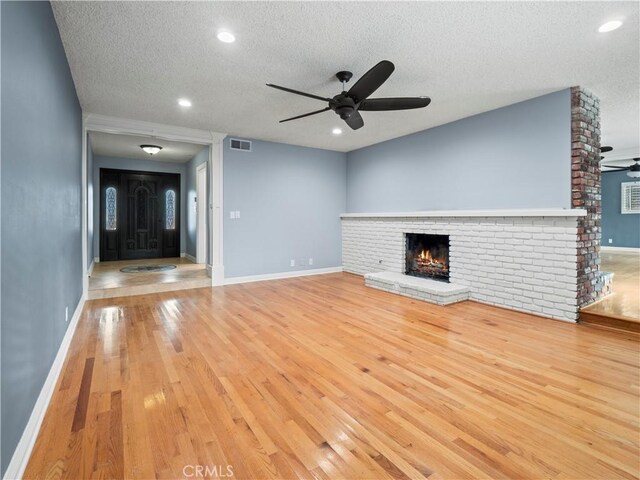 unfurnished living room featuring ceiling fan, light hardwood / wood-style floors, a brick fireplace, and a textured ceiling