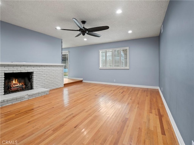 unfurnished living room featuring ceiling fan, a fireplace, light hardwood / wood-style floors, and a textured ceiling