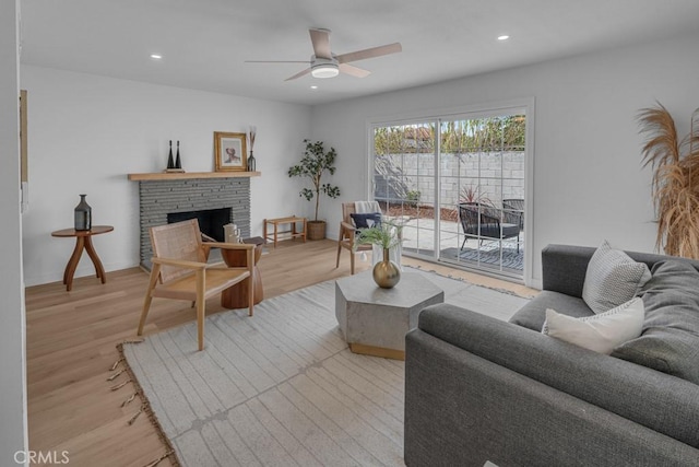 living area with a fireplace with raised hearth, ceiling fan, light wood finished floors, and recessed lighting