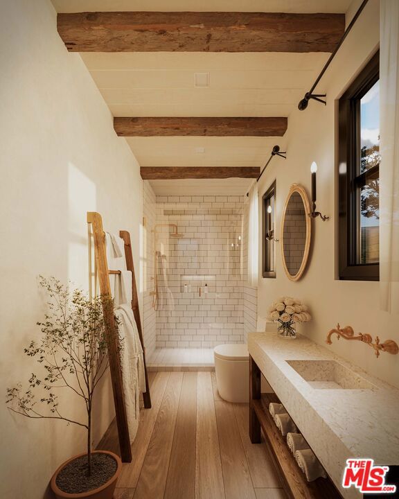 bathroom with sink, hardwood / wood-style floors, beam ceiling, a tile shower, and toilet