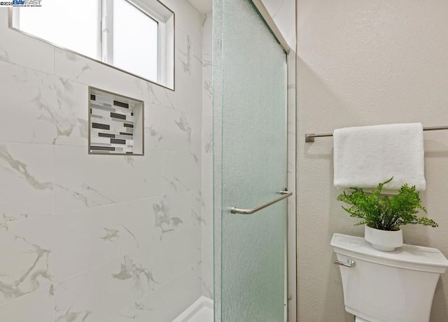 bathroom featuring a shower with shower door and toilet