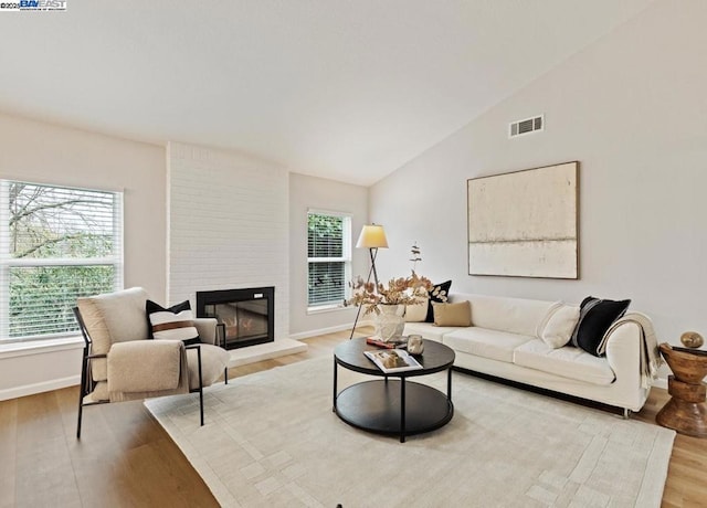 living room with vaulted ceiling, a brick fireplace, and light hardwood / wood-style flooring