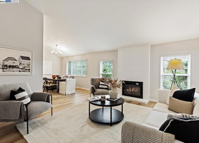 living room featuring a chandelier, a brick fireplace, and light wood-type flooring