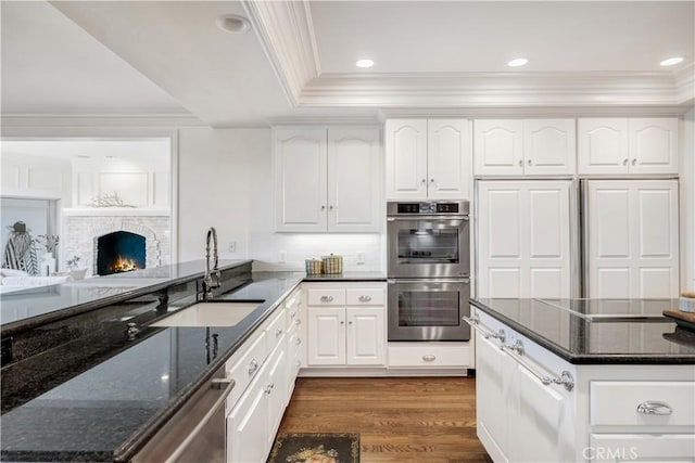 kitchen with appliances with stainless steel finishes, dark hardwood / wood-style floors, white cabinetry, sink, and dark stone counters