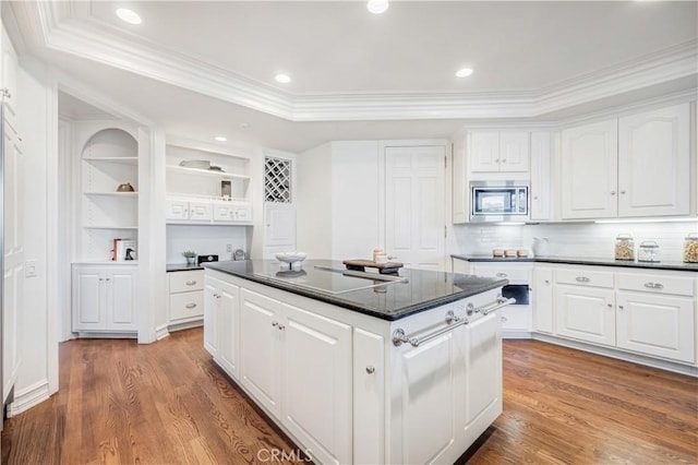 kitchen with hardwood / wood-style flooring, stainless steel microwave, a kitchen island, and white cabinets