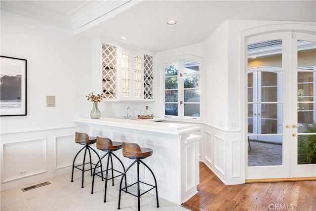 bar with white cabinetry, ornamental molding, sink, and light wood-type flooring