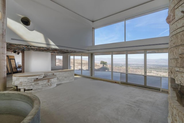 unfurnished living room with concrete flooring, a high ceiling, a mountain view, and a healthy amount of sunlight