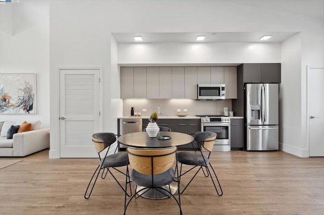 kitchen with light hardwood / wood-style flooring, gray cabinets, stainless steel appliances, tasteful backsplash, and vaulted ceiling