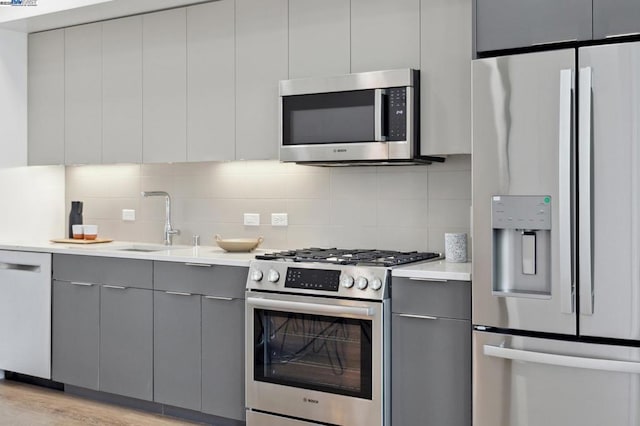 kitchen featuring sink, gray cabinetry, backsplash, stainless steel appliances, and light wood-type flooring