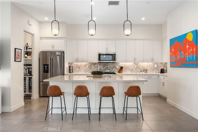 kitchen featuring a kitchen island with sink, white cabinetry, tasteful backsplash, and appliances with stainless steel finishes