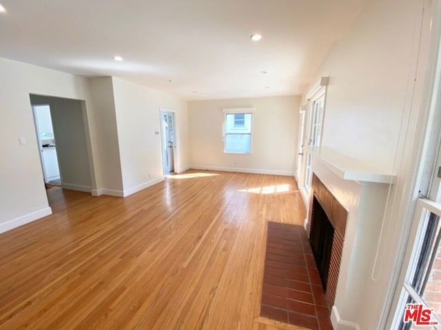 unfurnished living room with a brick fireplace and light hardwood / wood-style flooring