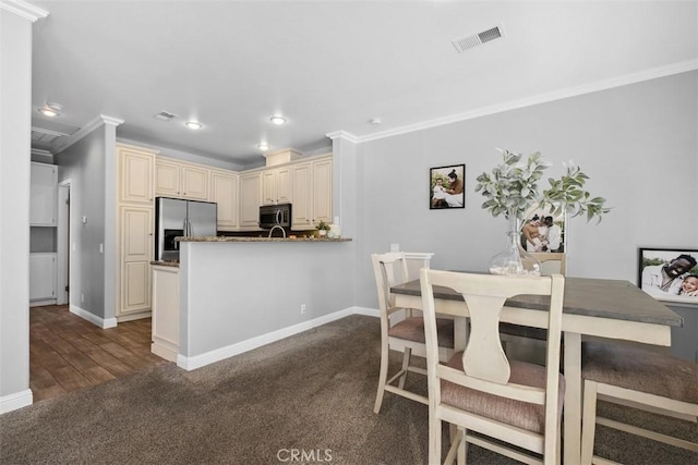 kitchen with crown molding, dark stone countertops, kitchen peninsula, stainless steel appliances, and cream cabinetry